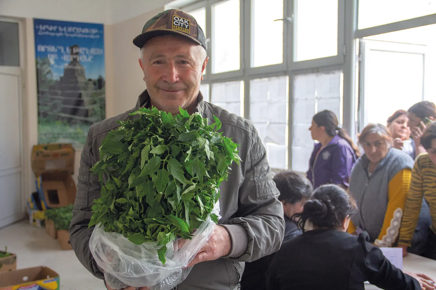 Armenak Markosyan, souriant, tient une botte de semis de légumes dans le bâtiment communal d’Angeghakot