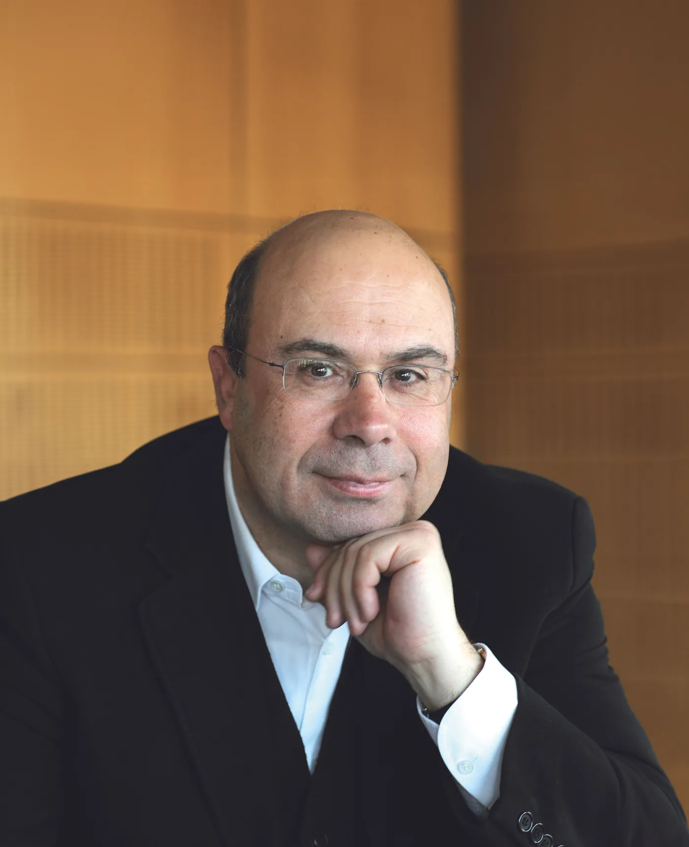 Portrait de Christian Makarian, lunettes et veste sombre, souriant, le menton appuyé sur la main